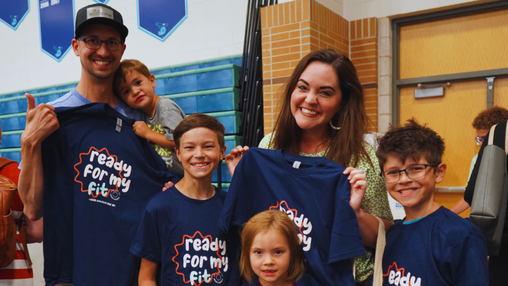 A smiling family holding up UEFA t shirts at the summer provider fair